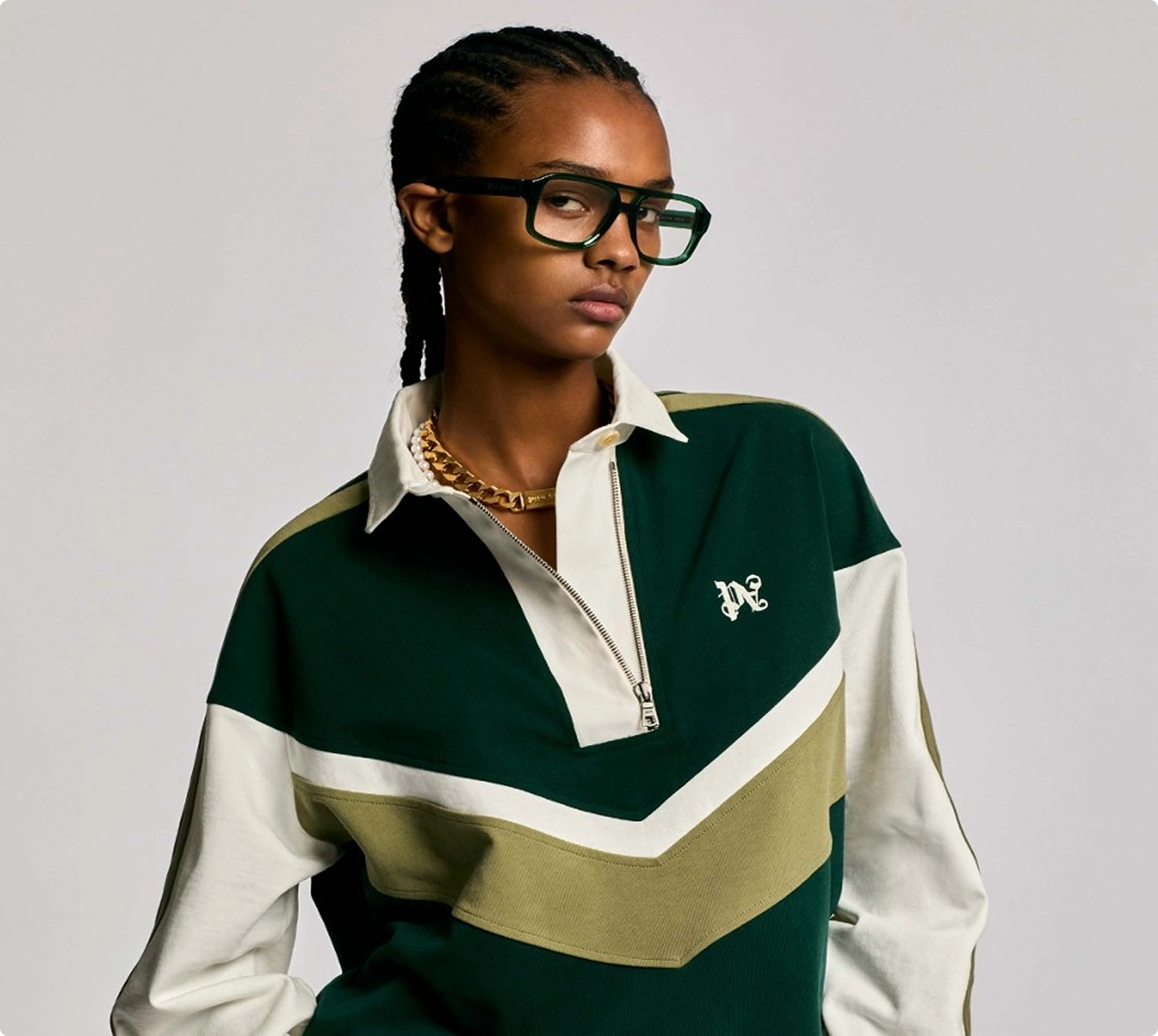 Person in stylish green and white polo shirt with glasses and braided hair, showcasing modern fashion.