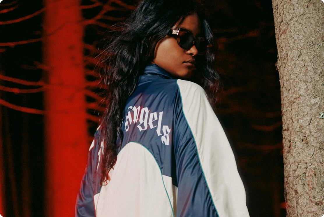 Stylish individual in sunglasses and a jacket, standing in a forest with red lighting ambiance.