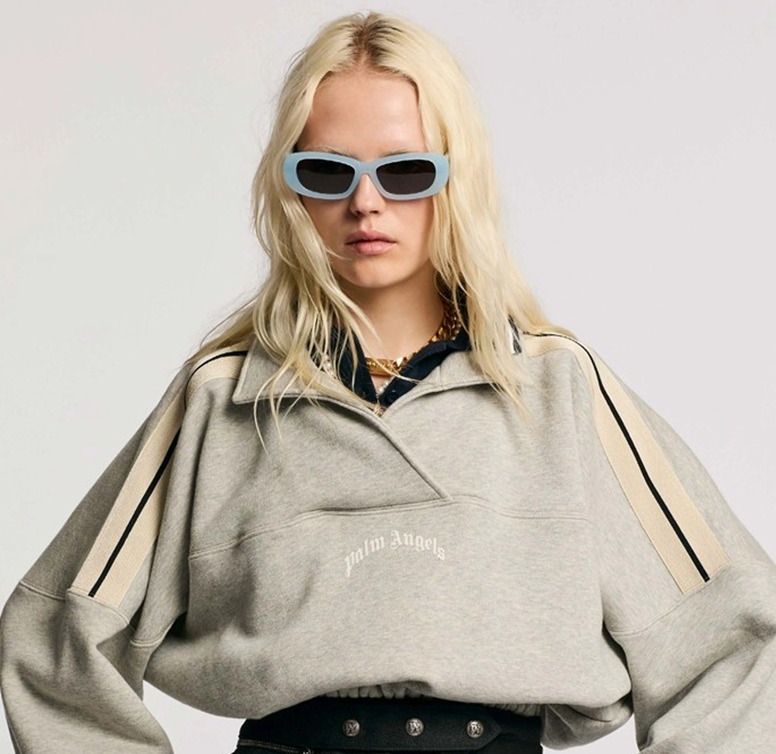 Fashionable woman in oversized grey sweater and blue sunglasses, exuding a modern, chic style.